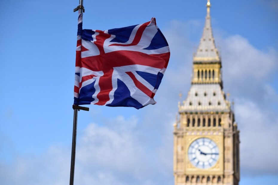 Union Jack flag waving in front of Big Ben, London, against a clear blue sky.