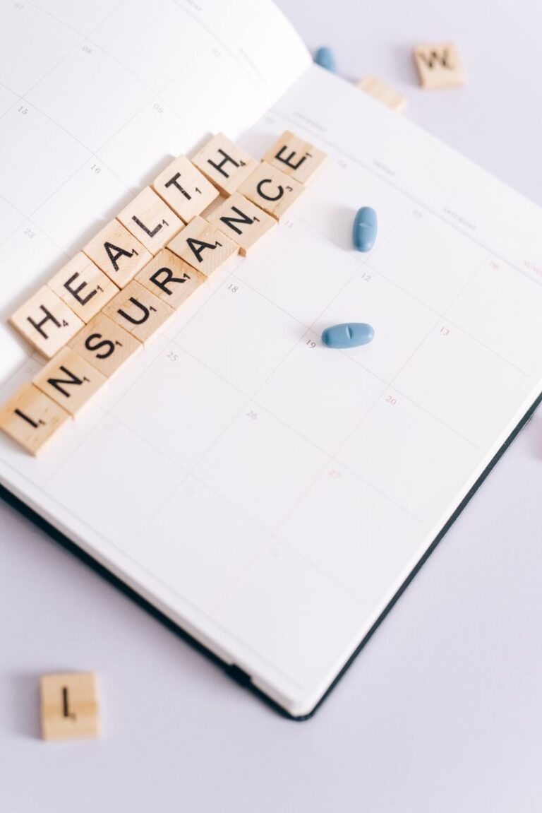 Scrabble tiles spelling 'health insurance' on a calendar beside blue pills, symbolizing medication schedule.