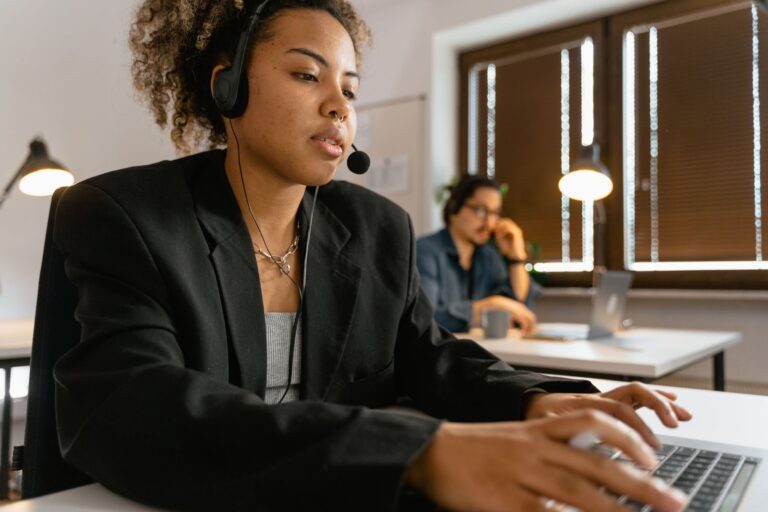Professional call center agent using headphones and laptop in an office setting.