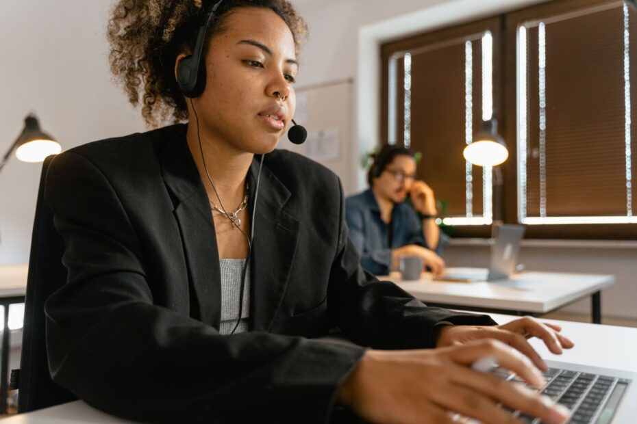 Professional call center agent using headphones and laptop in an office setting.