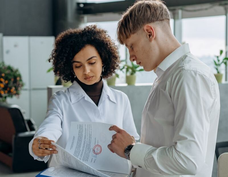 Two professionals discussing paperwork in a modern office setting.